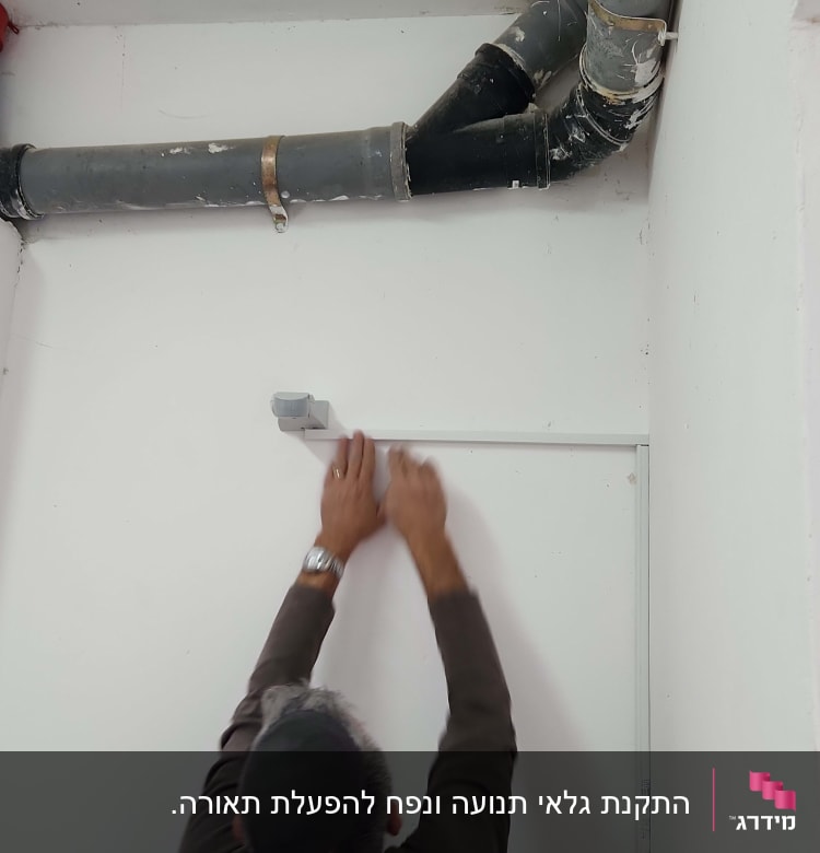 חשמלאי מתקין תעלה על קיר לבן
